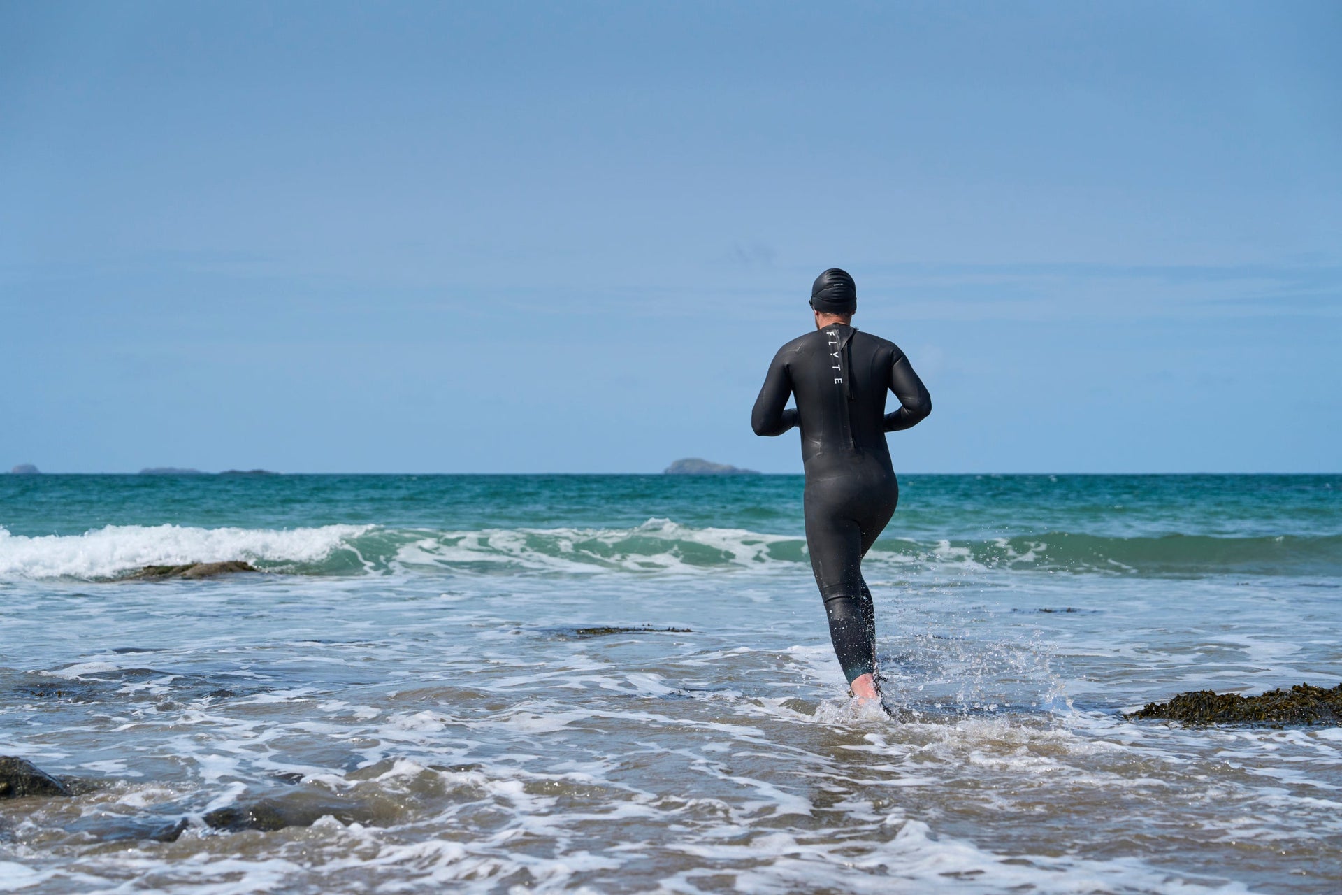 Person in a Flyte wetsuit entering the sea for open water swimming
